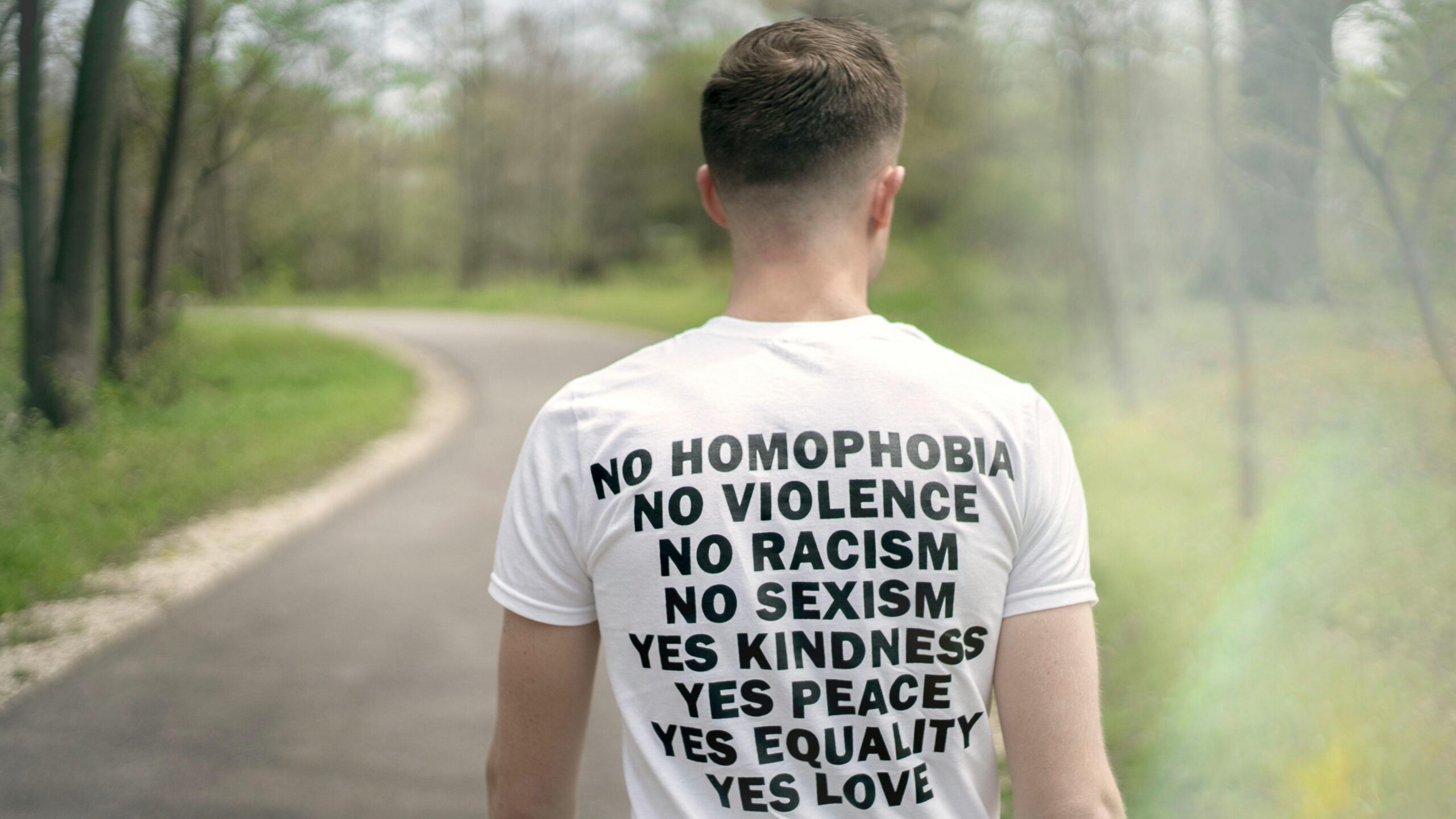 Man in a white T-shirt promoting equality and love during a peaceful walk outdoors.